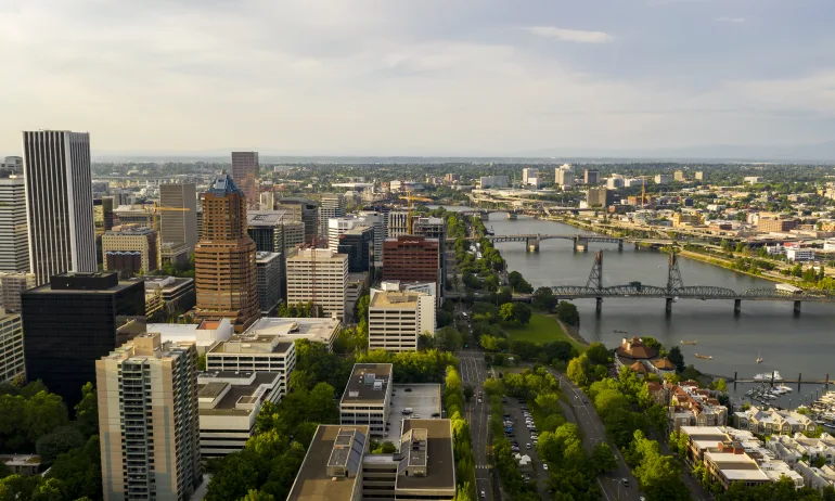 aerial view of downtown area with buildings and roadways, bridges crossing a river to a smaller set of buildings that expand into the distance