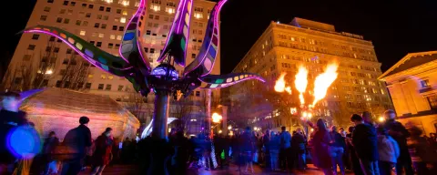 a crowd mingles under a fire display and a lighted purple sculpture