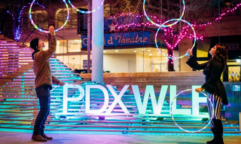 two people thrown lighted rings in front of a "PDXWLF" sign
